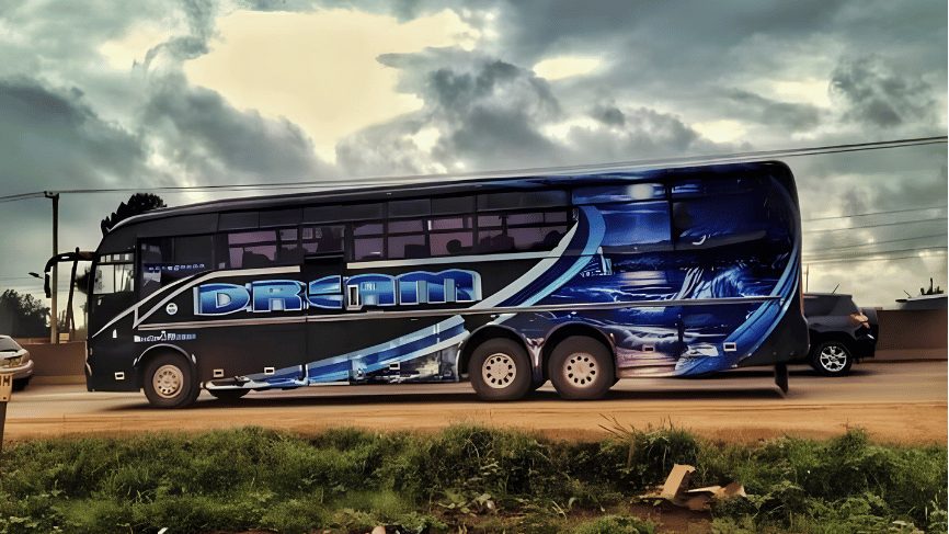 Side profile view of a black multi-axle Dreamline bus with blue graphic wave designs parked along a road under cloudy skies.