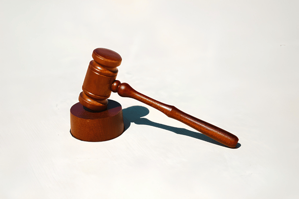 Wooden judge's gavel resting on a matching round sound block against a off-white background.