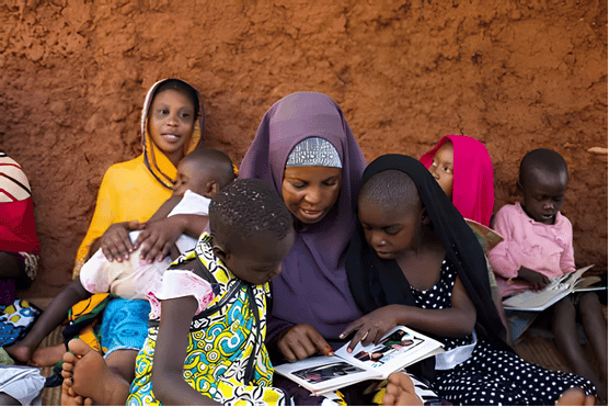 A mother wearing a hijab reading a book with her children seated outdoors, demonstrating parental involvement under the Basic Education Bill 2026.