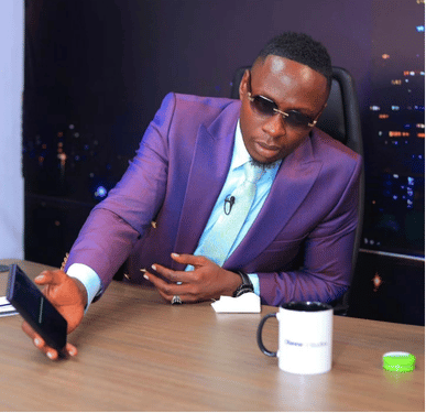 Oga Obinna holding a smartphone in studio while promoting the Verified Workers job site.