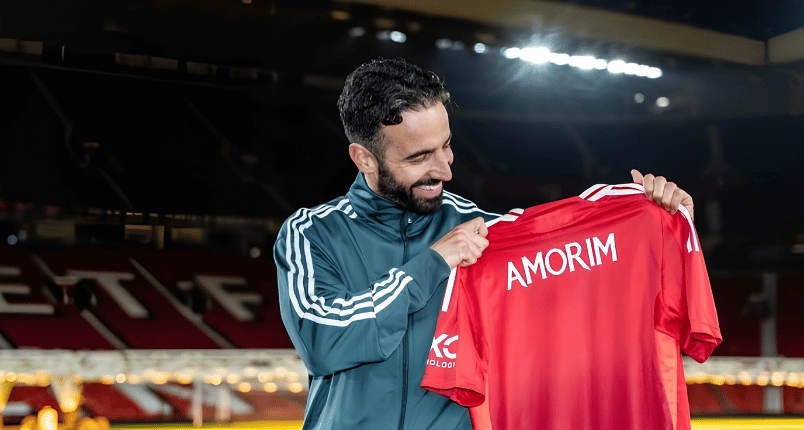 ormer Manchester United head coach Ruben Amorim smiling while holding a custom red jersey at Old Trafford.