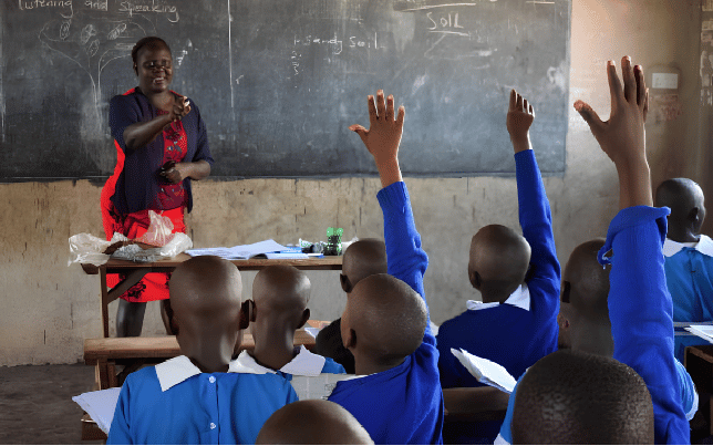 Female TSC teachers instructing primary school pupils raising their hands in a Kenyan classroom