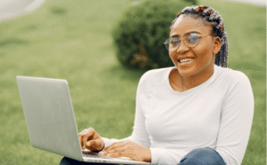 A young African woman sitting outdoors on green lawn grass working on her laptop on foreign dollar remote jobs opportunity in Kenya