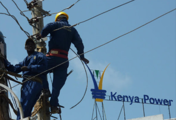 Kenya Power technicians climbing a utility pole to conduct line repairs near a Kenya Power logo sign.